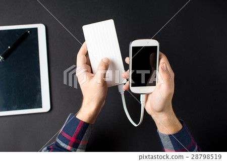 Man holding a white cellphone connected to a power bank Man holding a white cellphone connected to a power bank 28798519