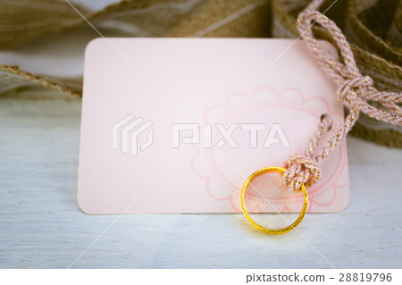 Blank pink paper card and gold ring on white wood 28819796