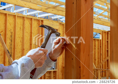 builder hammers a nail into a wooden beam builder hammers a nail into a wooden beam 28829726