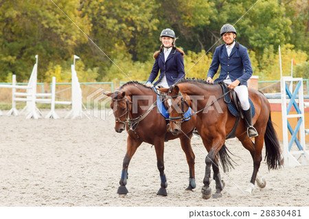 Young man and woman riding bay horses on field 28830481