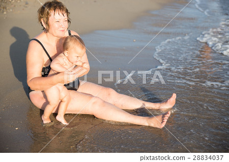 Naked baby on aged woman hands at beach 28834037