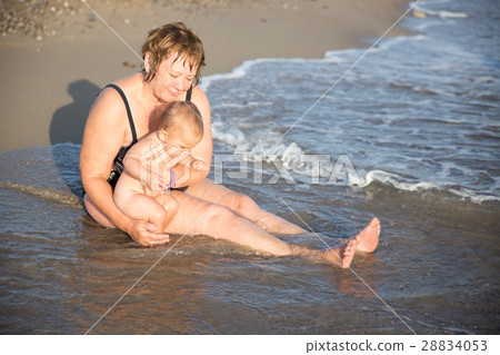 Naked baby on aged woman hands at beach Naked baby on aged woman hands at beach 28834053