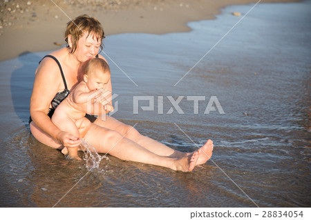Naked baby on aged woman hands at beach Naked baby on aged woman hands at beach 28834054