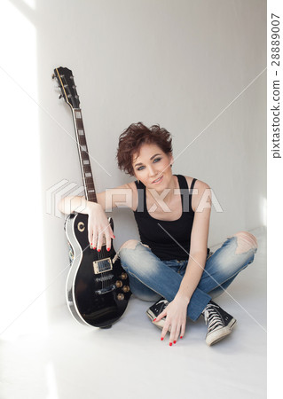 girl musician with a guitar sitting in white room 28889007