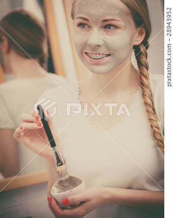 Happy young woman having mud mask on face 28943952