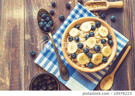 Oatmeal with blueberries and banana in wooden bowl Oatmeal with blueberries and banana in wooden bowl 28976223