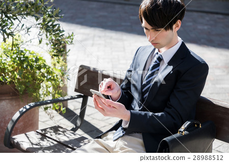 A man watching a smartphone on a bench 28988512