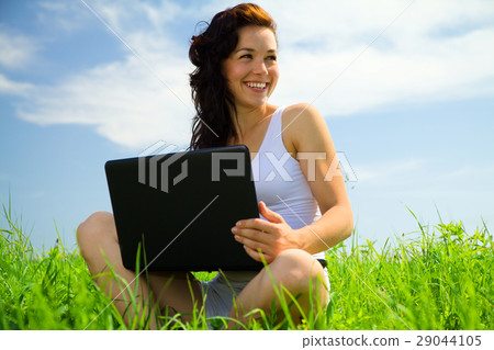 Cute girl is sitting on green grass with laptop 29044105