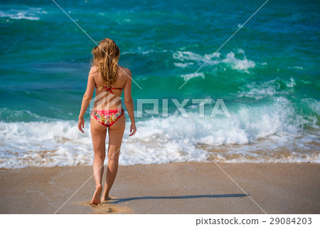 Beautiful young woman walking on ocean shore 29084203