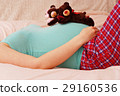 Young pregnant mother lies with soft toy of their future baby 29160536