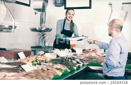 Friendly shopgirl offering fish to client. 29164316