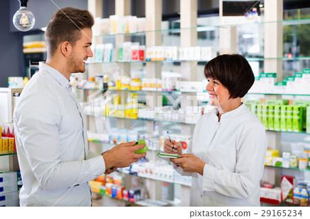 Woman pharmacist helping customers in drug store 29165234