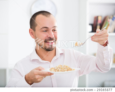 Positive young man eating porridge Positive young man eating porridge 29165877