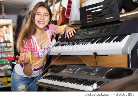 Smiling positive young girl choosing synthesizer Smiling positive young girl choosing synthesizer 29165895