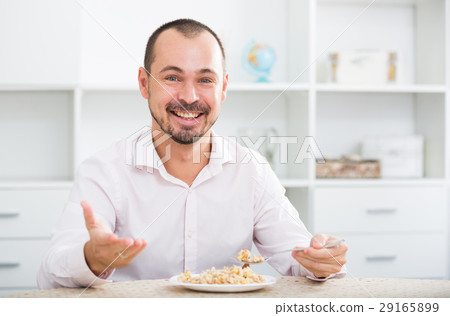 Positive young man eating porridge Positive young man eating porridge 29165899