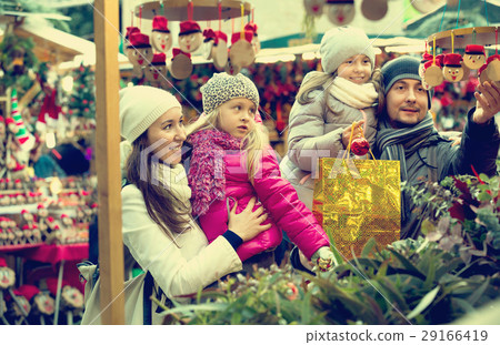 Smiling cheerful family of four buying Caga Tio. Focus on woman Smiling cheerful family of four buying Caga Tio. Focus on woman 29166419