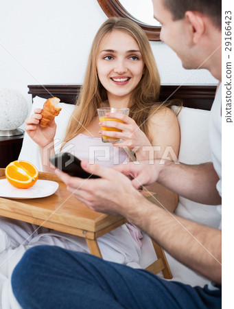 Young positive couple reading news from smartphone Young positive couple reading news from smartphone 29166423