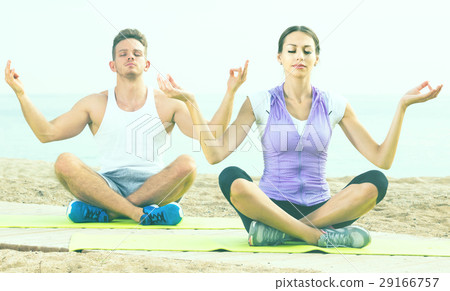 Cross-legged couple practice yoga on beach in morning 29166757