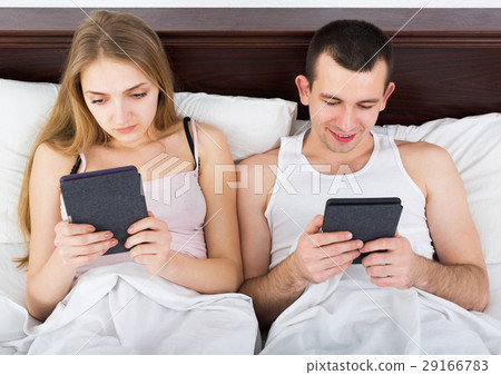 Young couple reading news from e-readers in bed 29166783
