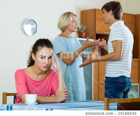 Sad young woman watching husband and mother having fight Sad young woman watching husband and mother having fight 29166836