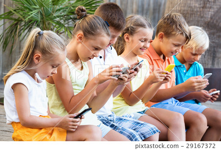Busy children holding smartphones and sitting Busy children holding smartphones and sitting 29167372