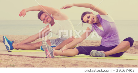 guy and girl practising yoga poses sitting on beach by sea at daytime 29167402