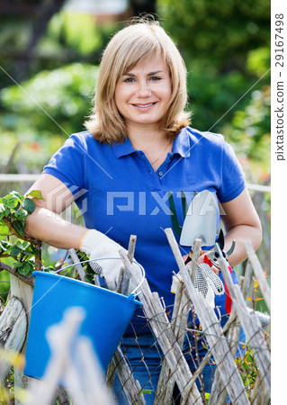 Smiling woman holding horticultural tools in garden on sunny day Smiling woman holding horticultural tools in garden on sunny day 29167498