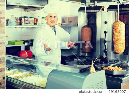 man chef wearing uniform cutting meat for kebab on kitchen in fa man chef wearing uniform cutting meat for kebab on kitchen in fa 29168907