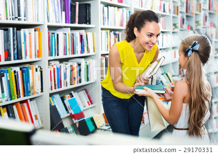 Woman giving book to girl in school age in bookstore Woman giving book to girl in school age in bookstore 29170331