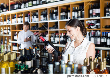 Happy young woman choosing bottle in wine shop Happy young woman choosing bottle in wine shop 29170393