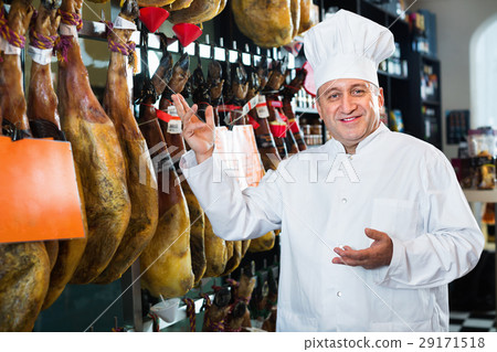 Portrait of mature shop man offering Spanish jamon 29171518