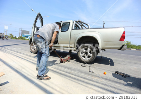 A man changing the wheel at the side of the road A man changing the wheel at the side of the road 29182313
