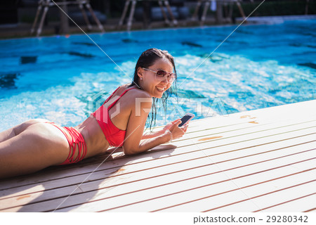 Beautiful woman leaning on poolside and typing a 29280342