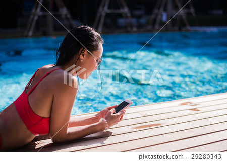 Beautiful woman leaning on poolside and typing a 29280343