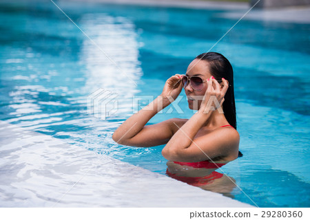 Woman wearing red swimsuit and sunglasses sitting 29280360