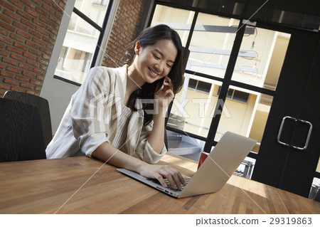 The woman is working with her laptop and talking on the phone at the same time The woman is working with her laptop and talking on the phone at the same time 29319863