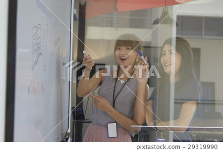 young woman standing near whiteboard and explaining new strategy with her colleagues. 29319990