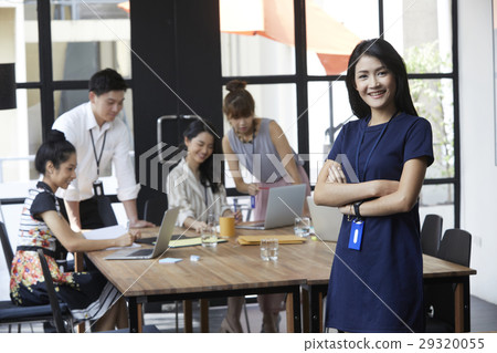 The businesswoman is smiling while colleagues are discussing. 29320055