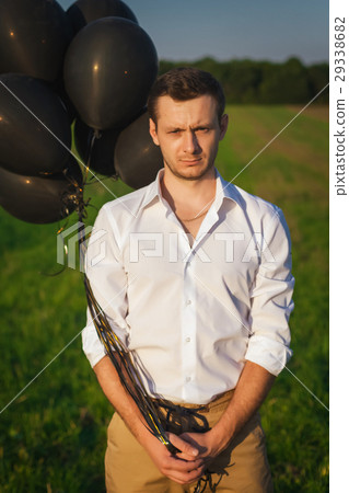 guy in white shirt with black balloons standing in 29338682