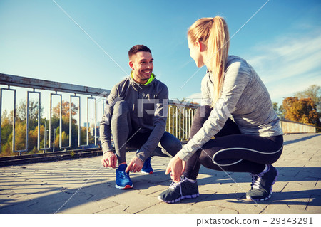 smiling couple tying shoelaces outdoors smiling couple tying shoelaces outdoors 29343291