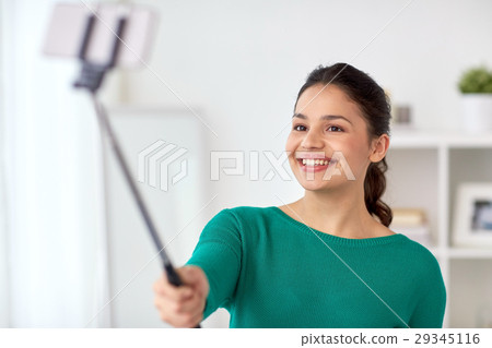 woman taking selfie by smartphone monopod at home 29345116