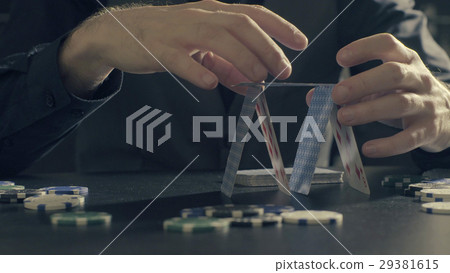 Man's hands building a house of a playing cards Man's hands building a house of a playing cards 29381615