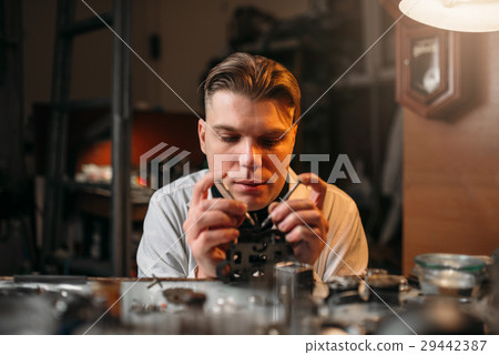 Watchmaker holding with tweezers a gear of hours Watchmaker holding with tweezers a gear of hours 29442387