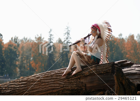 Young woman in war bonnet headdress of American Indian plays on a tree a flute Young woman in war bonnet headdress of American Indian plays on a tree a flute 29465121