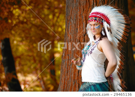 Young woman in war bonnet headdress of American Indian smokes a pipe 29465136