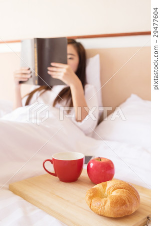 Woman reading book and drinking coffee on bed during the mornin Woman reading book and drinking coffee on bed during the mornin 29477604