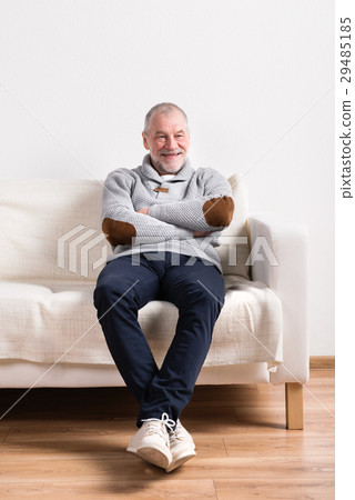 Senior man in gray sweater sitting on sofa, studio 29485185