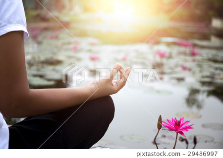 Woman doing yoga meditation next to lotus pond Woman doing yoga meditation next to lotus pond 29486997