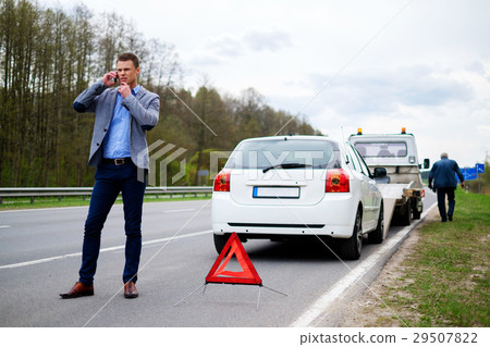 Man calling while tow truck picking up his broken 29507822