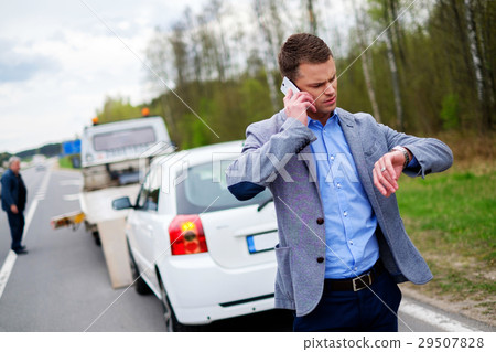Man calling while tow truck picking up his broken 29507828